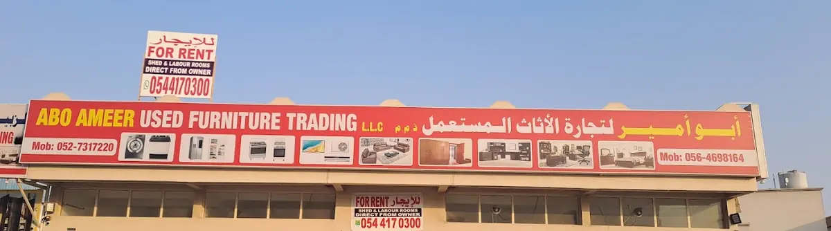 The shop sign: Abo Ameer Used Furniture Trading L.L.C., in English and Arabic, with icons of furniture and appliances